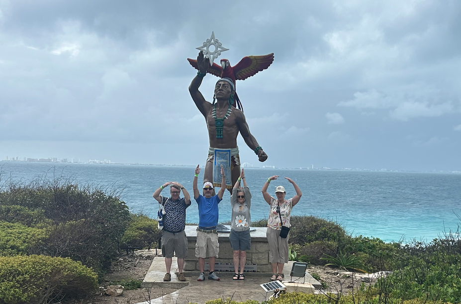 four older adults standing in front of a native american statue in front of a body of water using their arms to spell the word OHIO