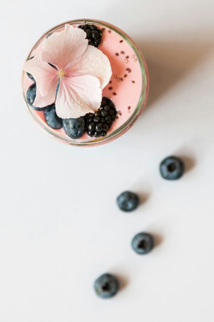 aerial view of a pink smoothie in a glass topped with berries and a flower